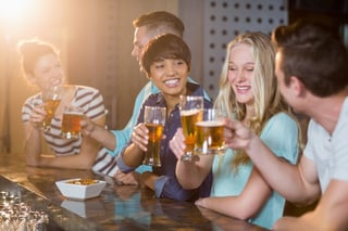 Group of smiling friends toasting glass of beer at counter in bar.jpeg