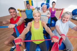 Portrait of happy men and women on fitness balls exercising with resistance bands in gym class.jpeg